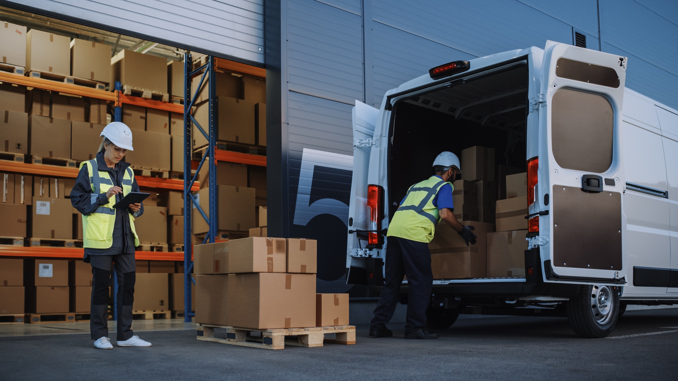 Outside of Logistics Distributions Warehouse With Inventory Manager Using Tablet Computer, talking to Worker Loading Delivery Truck with Cardboard Boxes. Online Orders, Purchases, E-Commerce Goods